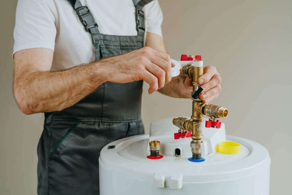 worker overalls wrapping plumbing tape around water heater pipe